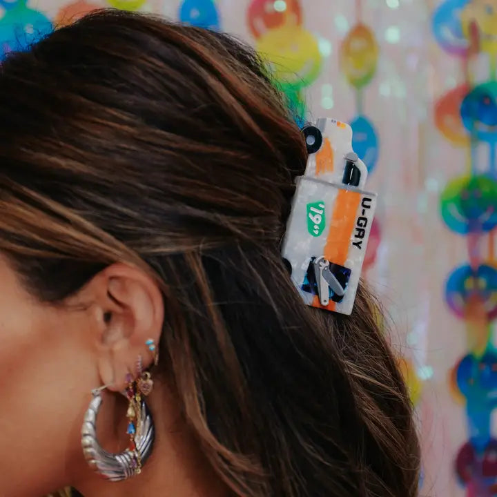 Close-up of a person wearing the moving truck shaped hair claw against a multicolored background.