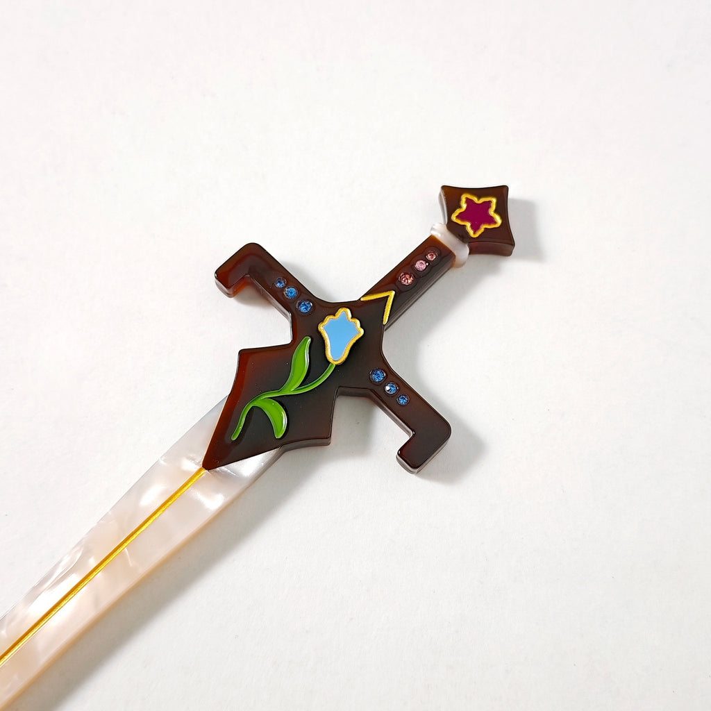 Close up of the brown hilt featuring a blue flower, blue and pink rhinestones, and a purple flower at the top against a white background.