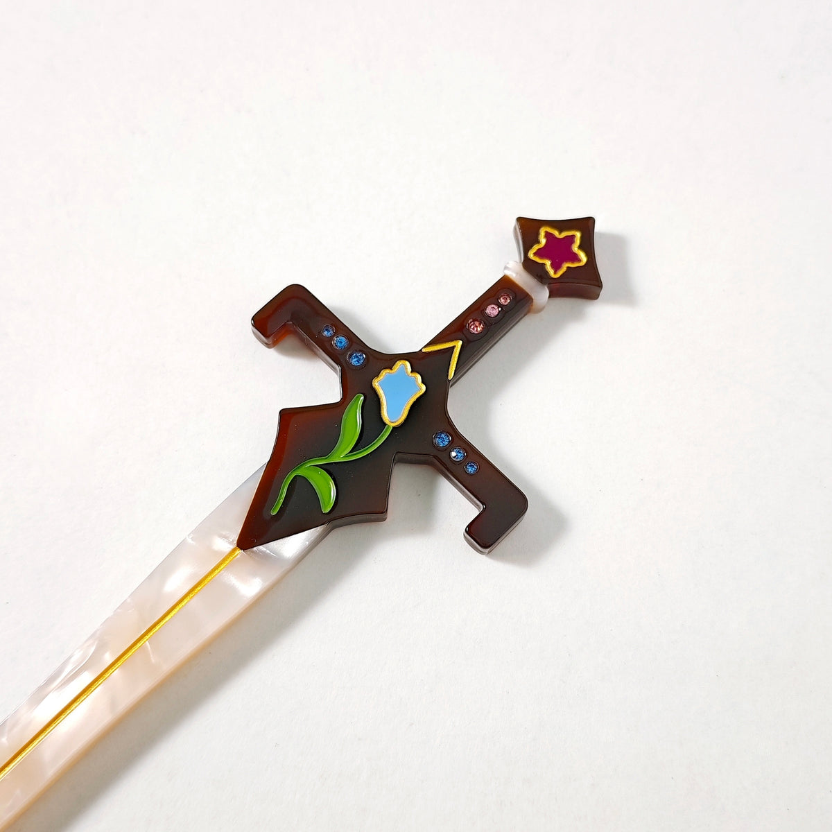 Close up of the brown hilt featuring a blue flower, blue and pink rhinestones, and a purple flower at the top against a white background.