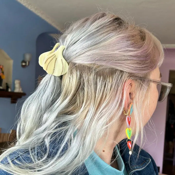 Person with pastel hair and colorful earrings, wearing the garlic bulb shaped hair claw.