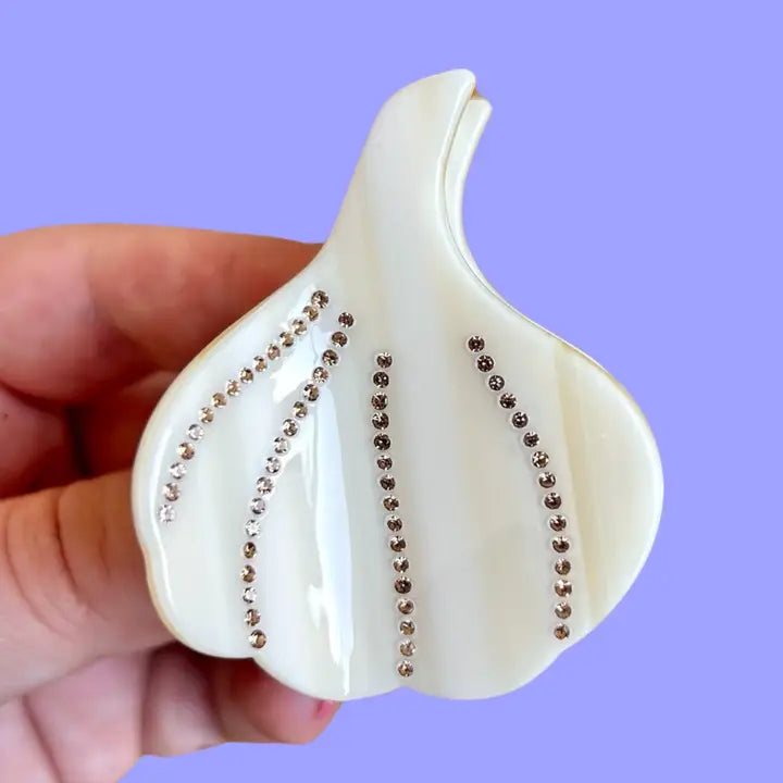 Hand holding the garlic bulb shaped hair claw with clear rhinestones on a purple background