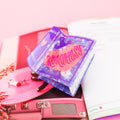 Marbled purple book hair claw with a silver sword going through a peach colored heart and the phrase 'Romantasy' in red lettering. Hair claw is resting on on an open magazine page featuring a pink vinyl record player.