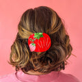 Brunette model wearing hair barrette against a pink background.