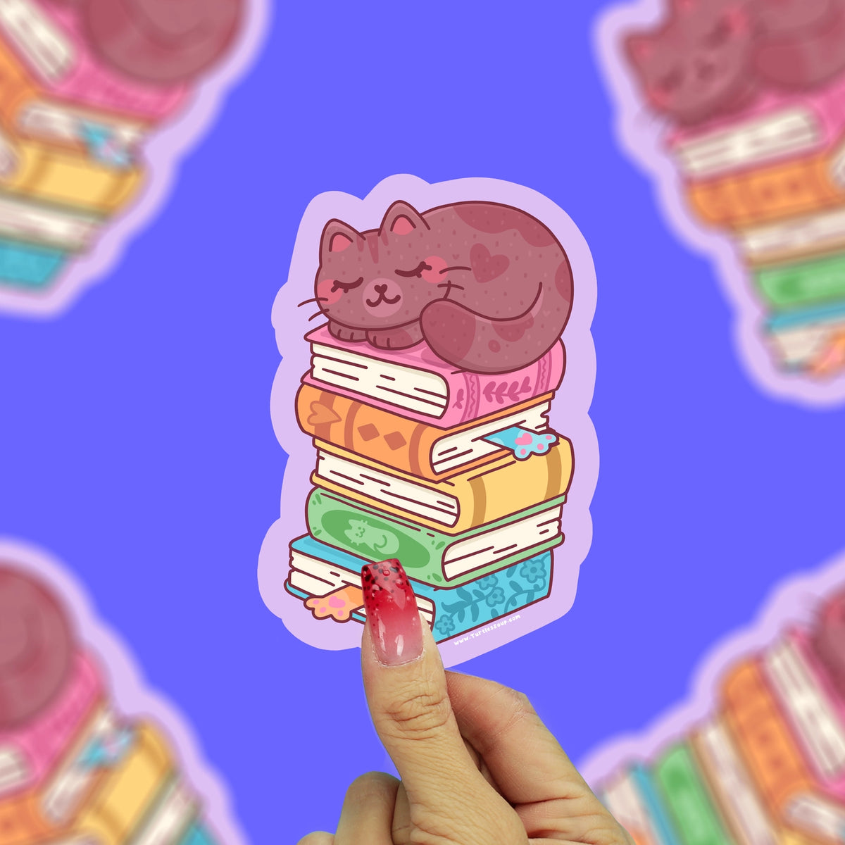 Brown cat sleeping on top of a stack of books. Books are pink, orange, yellow, green, and blue.