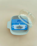 Hair clip on a blue packaging inside of a white dish against a cream background.