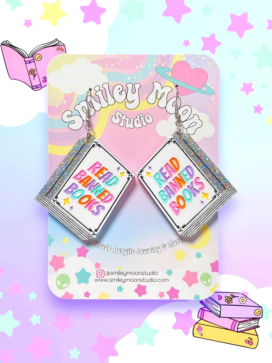 White book earrings with glitter spine and the phrase "Read Banned  Books" in a multi colored font on a jewelry tag against a colorful background.