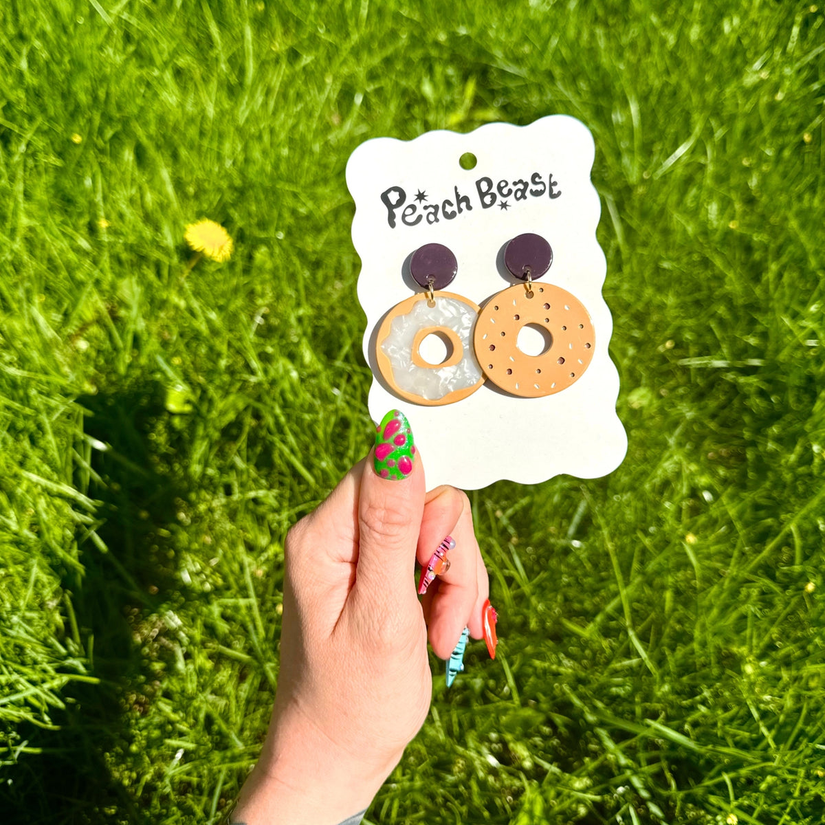 Bagel earrings on a ehite backing hard held by a hand against greenery.