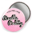 Mirror with "You're Like Really Pretty" in white and black lettering on pink with a second mirror behind it facing with mirror out against a white background.