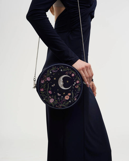 Model in a dark dress wearing the purse at their side against a white background.