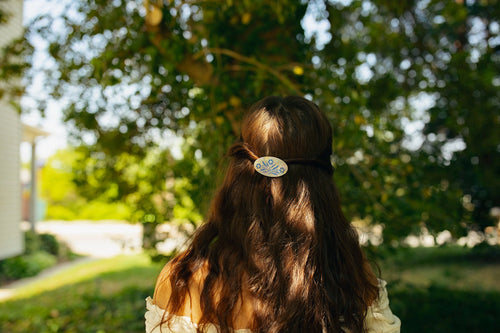 Brunette model wearing hair clip against a wooded background.