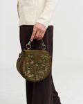 Model holding green saddle bag by short handle against a white background.