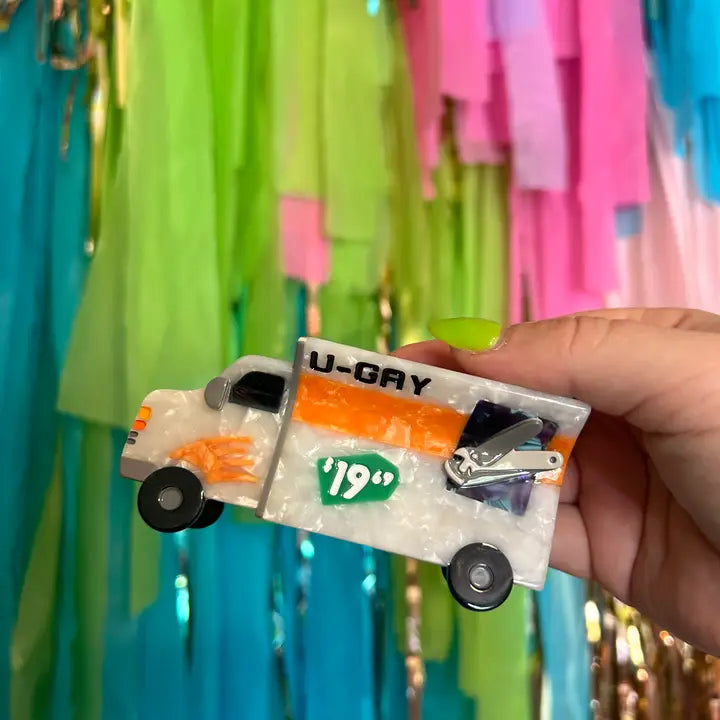 Moving truck shaped hair claw held by a hand with a colorful, blurred background
