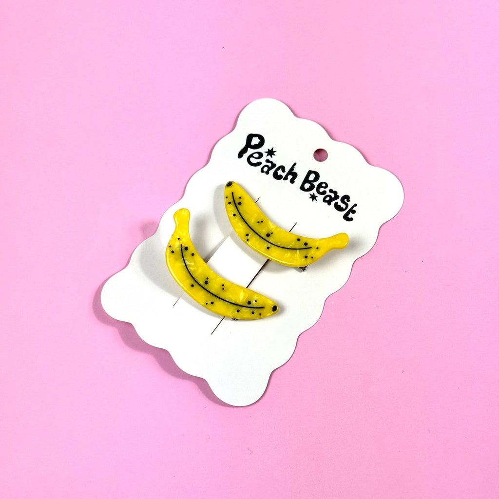 Two ripe banana clips on a white hang card against a pink background.