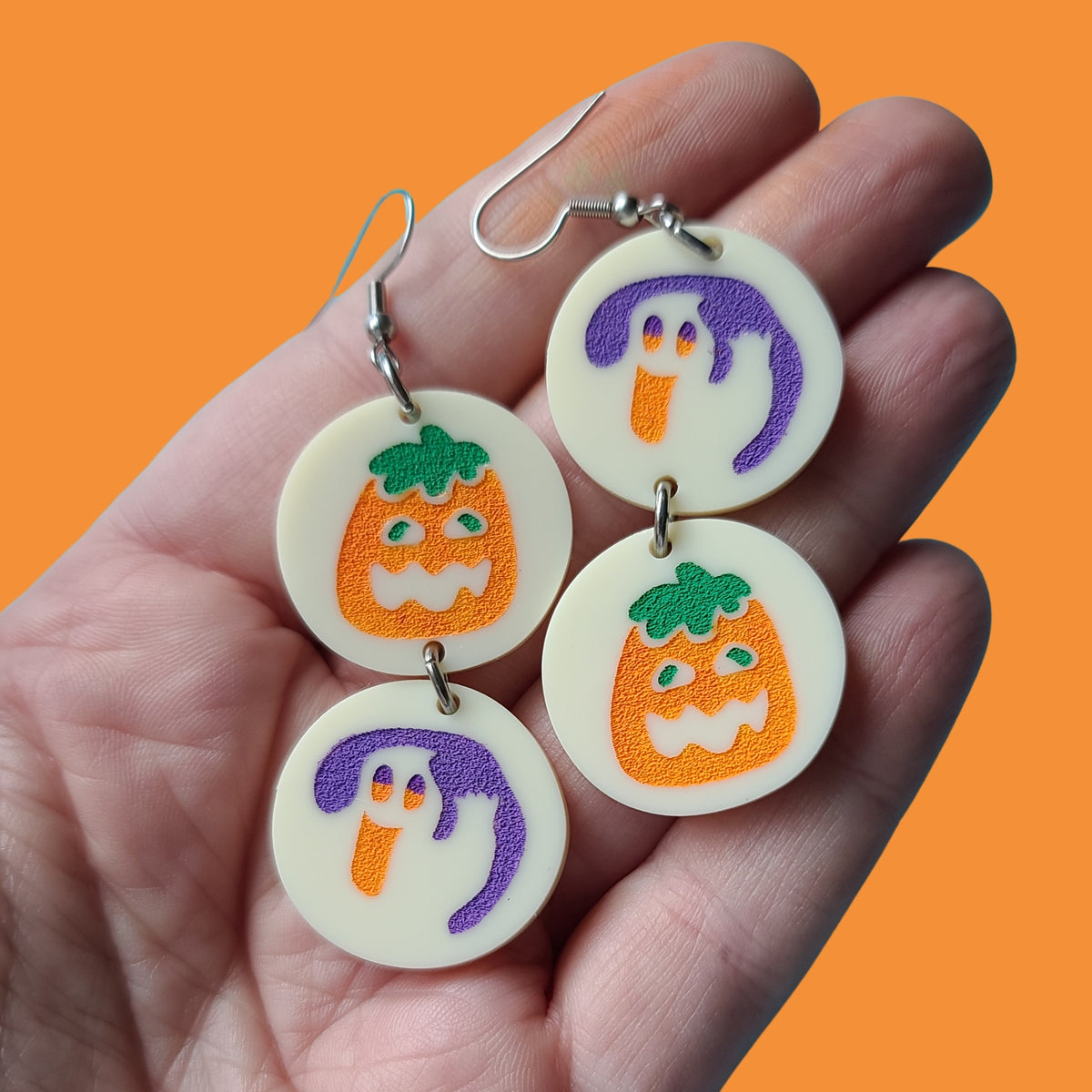 Hand holding earrings against orange background