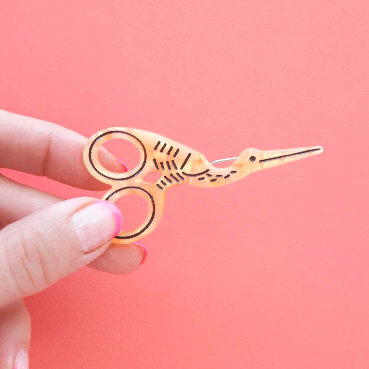 Model hand holding stork scissor hair barrette against a pink background.