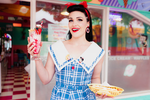 Female model wearing brooch while holding a milkshake and a hot dog